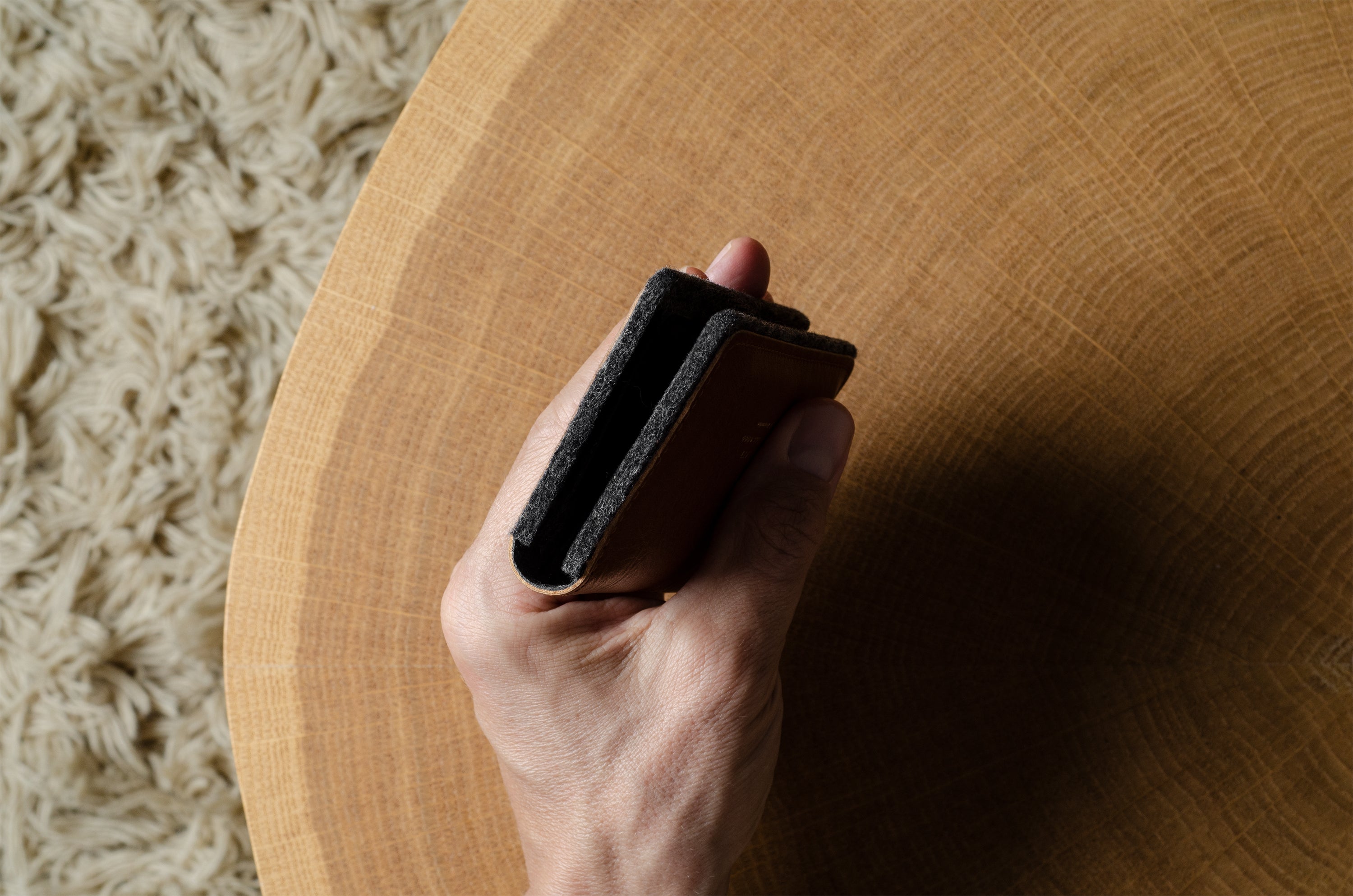 Hand holding a wallet on a wooden surface with a textured beige rug in the background