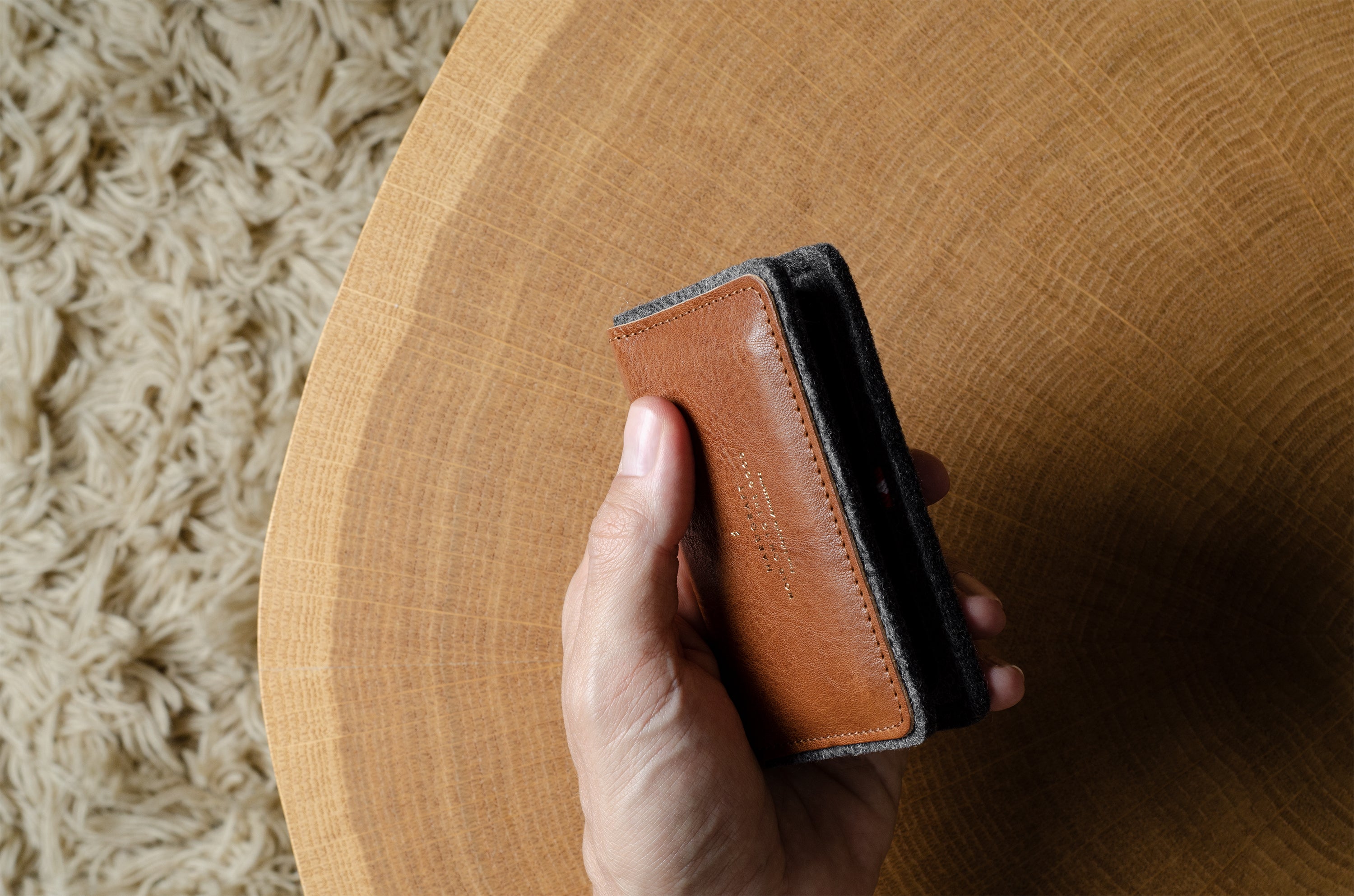 Hand holding a brown leather wallet on a wooden surface