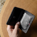 Hand holding a black and gray wallet on a wooden surface