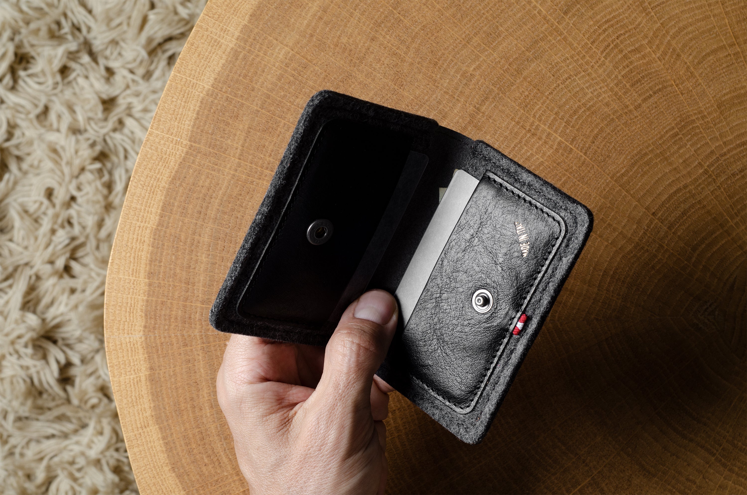 Hand holding a black and gray wallet on a wooden surface