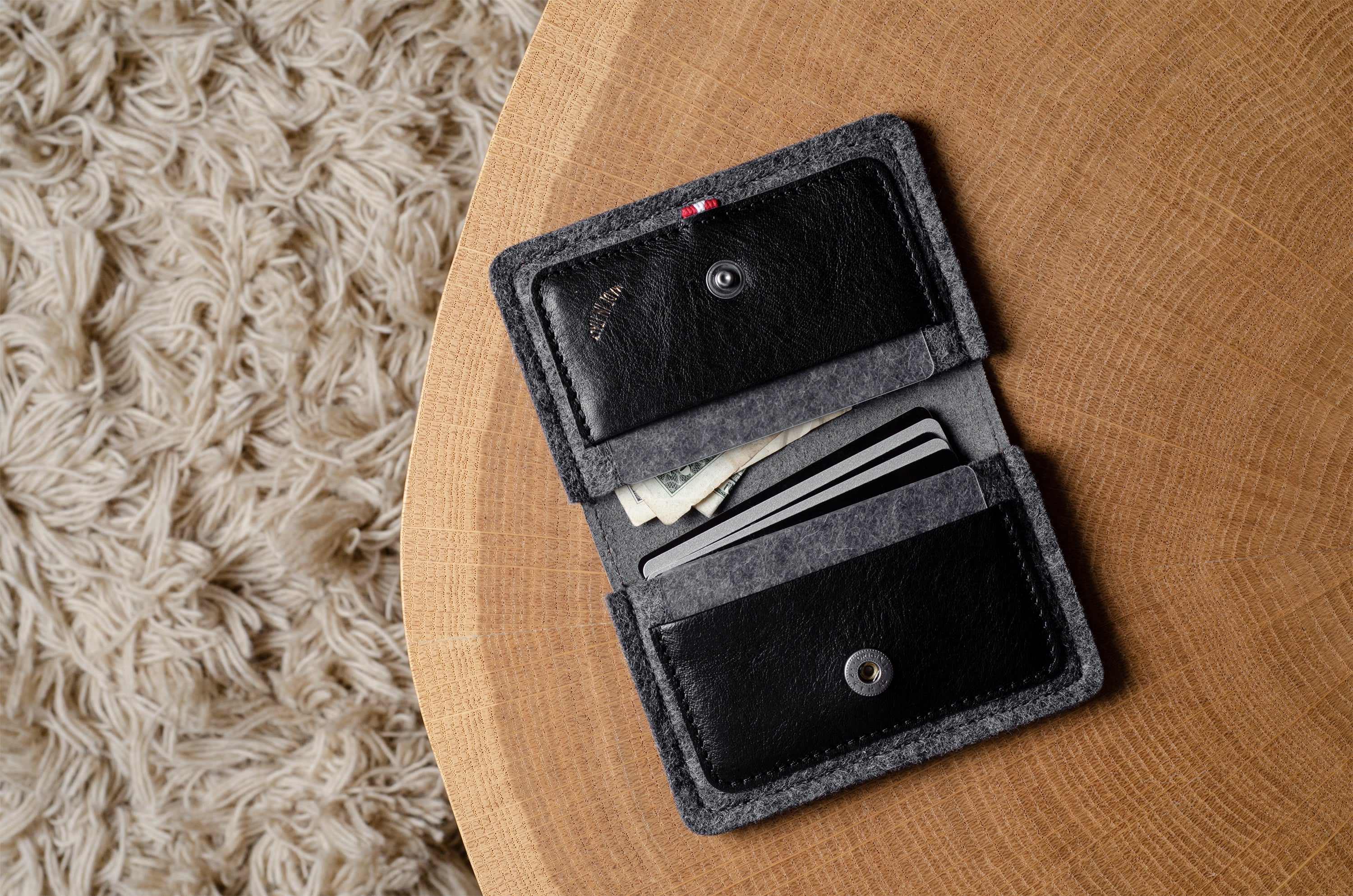 Open black felt wallet with coins and cards on a wooden surface