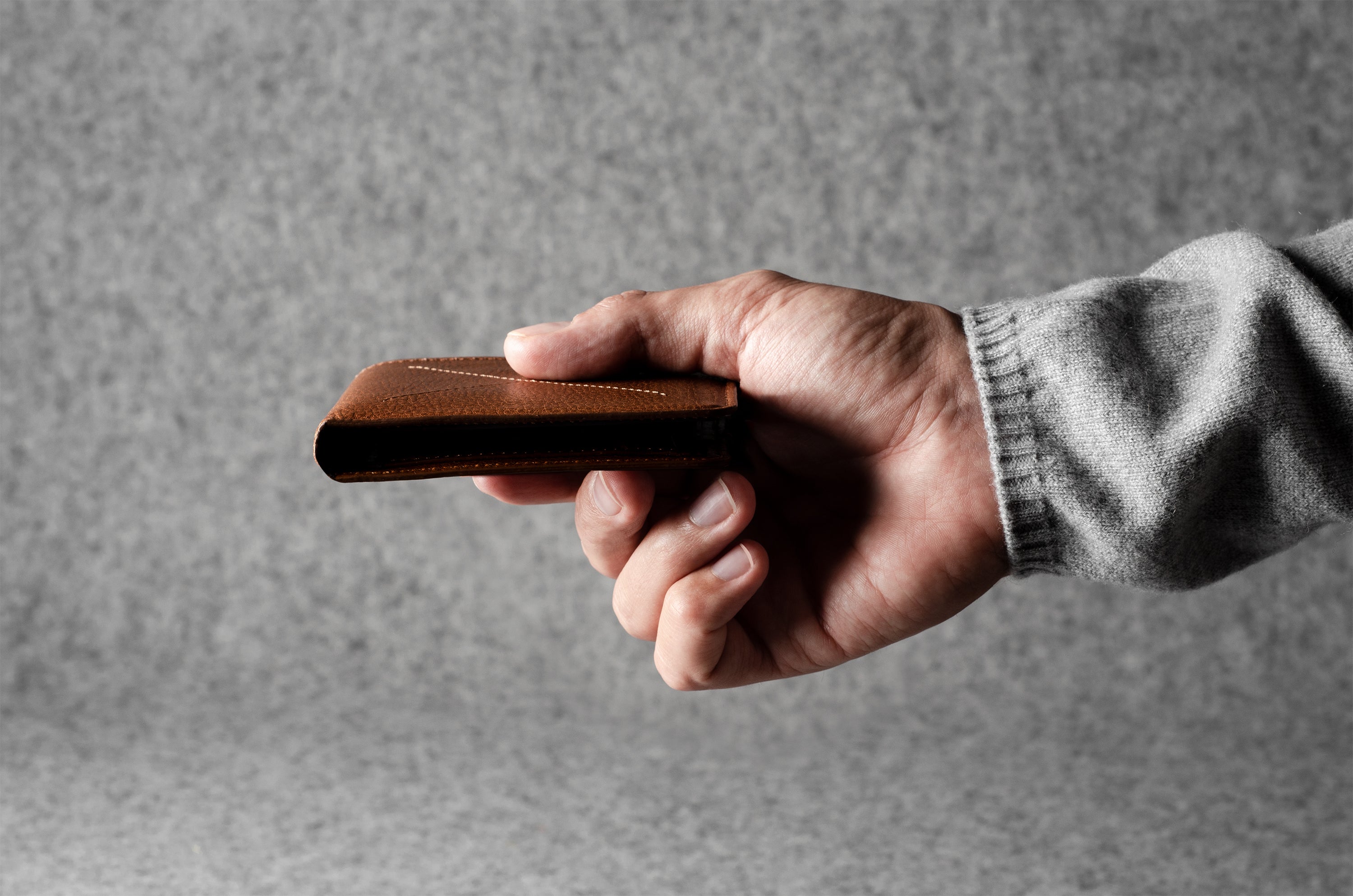 Hand holding a brown leather wallet against a gray background