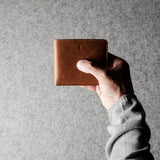 Hand holding a brown leather wallet against a gray background