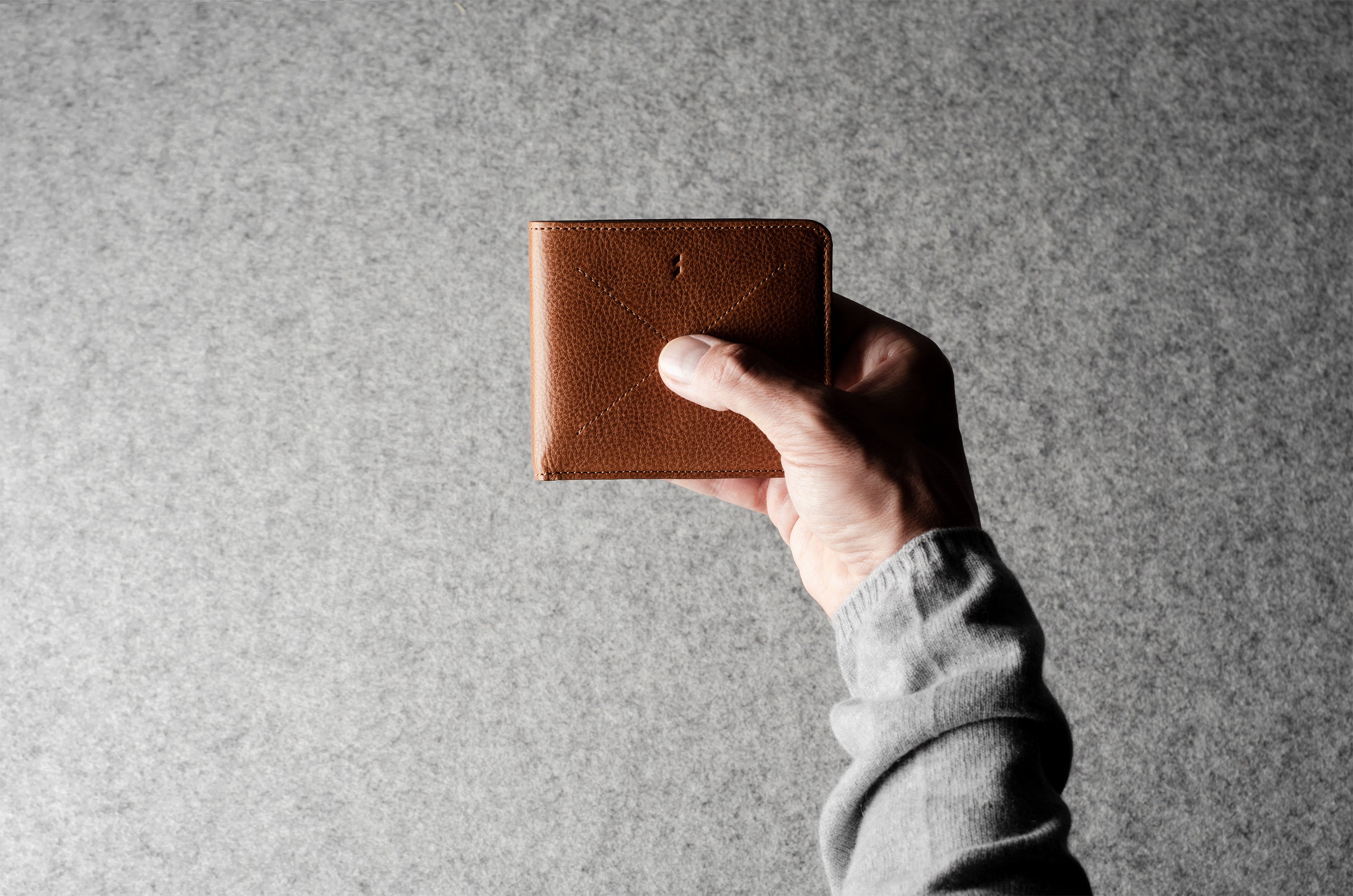 Hand holding a brown leather wallet against a gray background