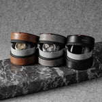 Three watch cases on a marble surface with a neutral background