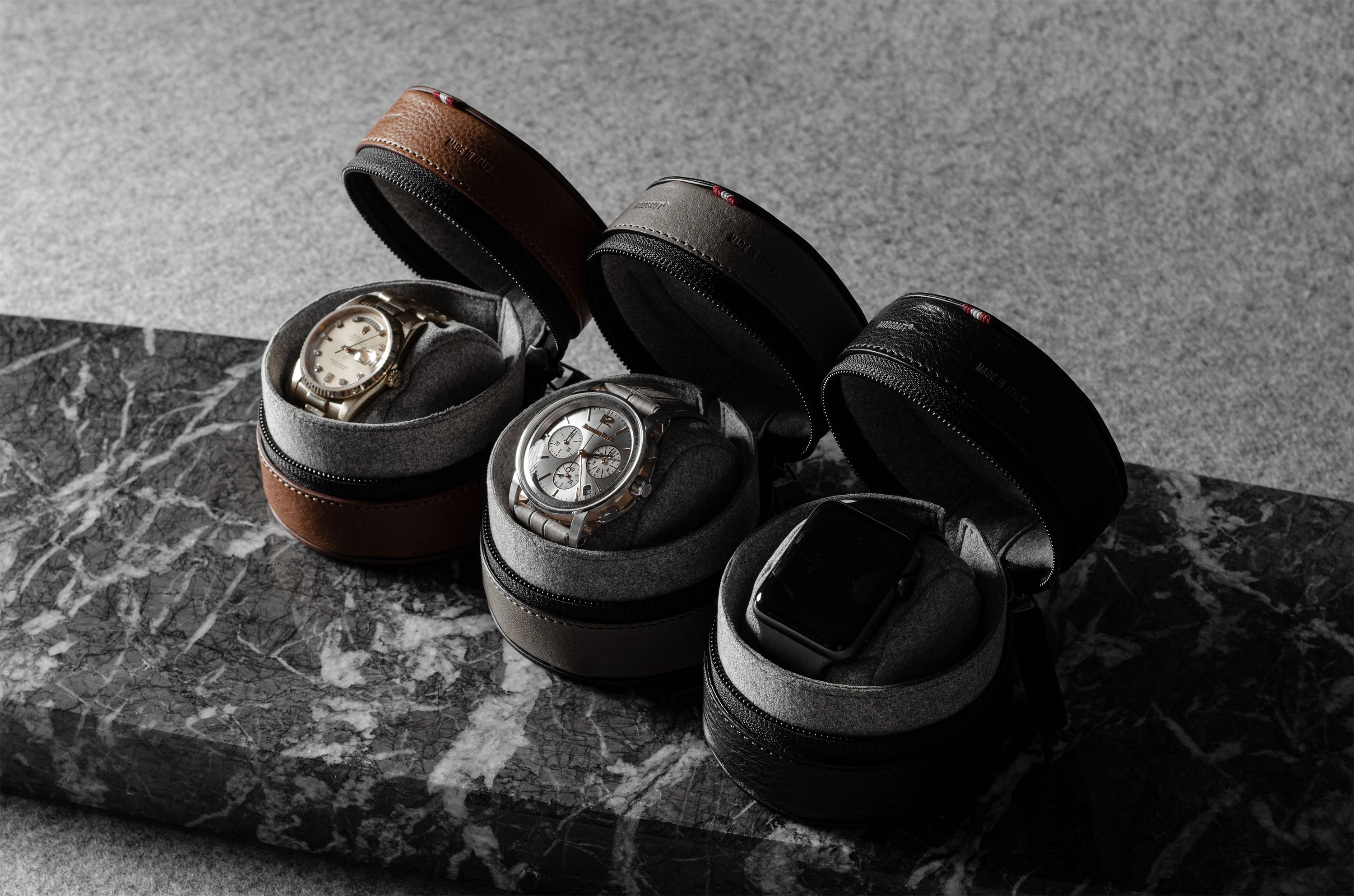 Set of three watch cases with watches on a marble surface