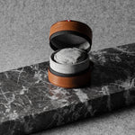 Brown leather watch case with gray interior on a marble surface