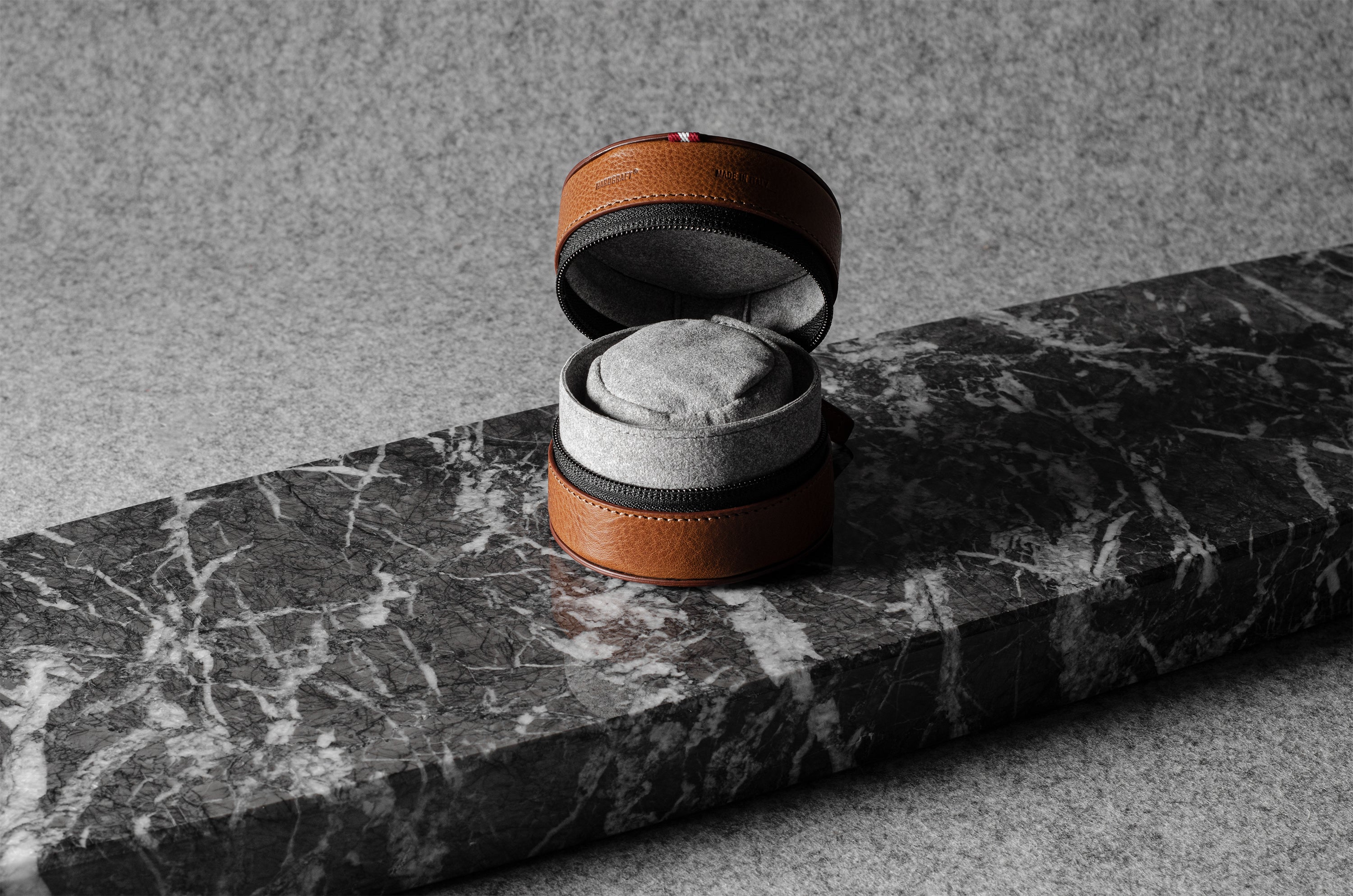 Brown leather watch case with gray interior on a marble surface