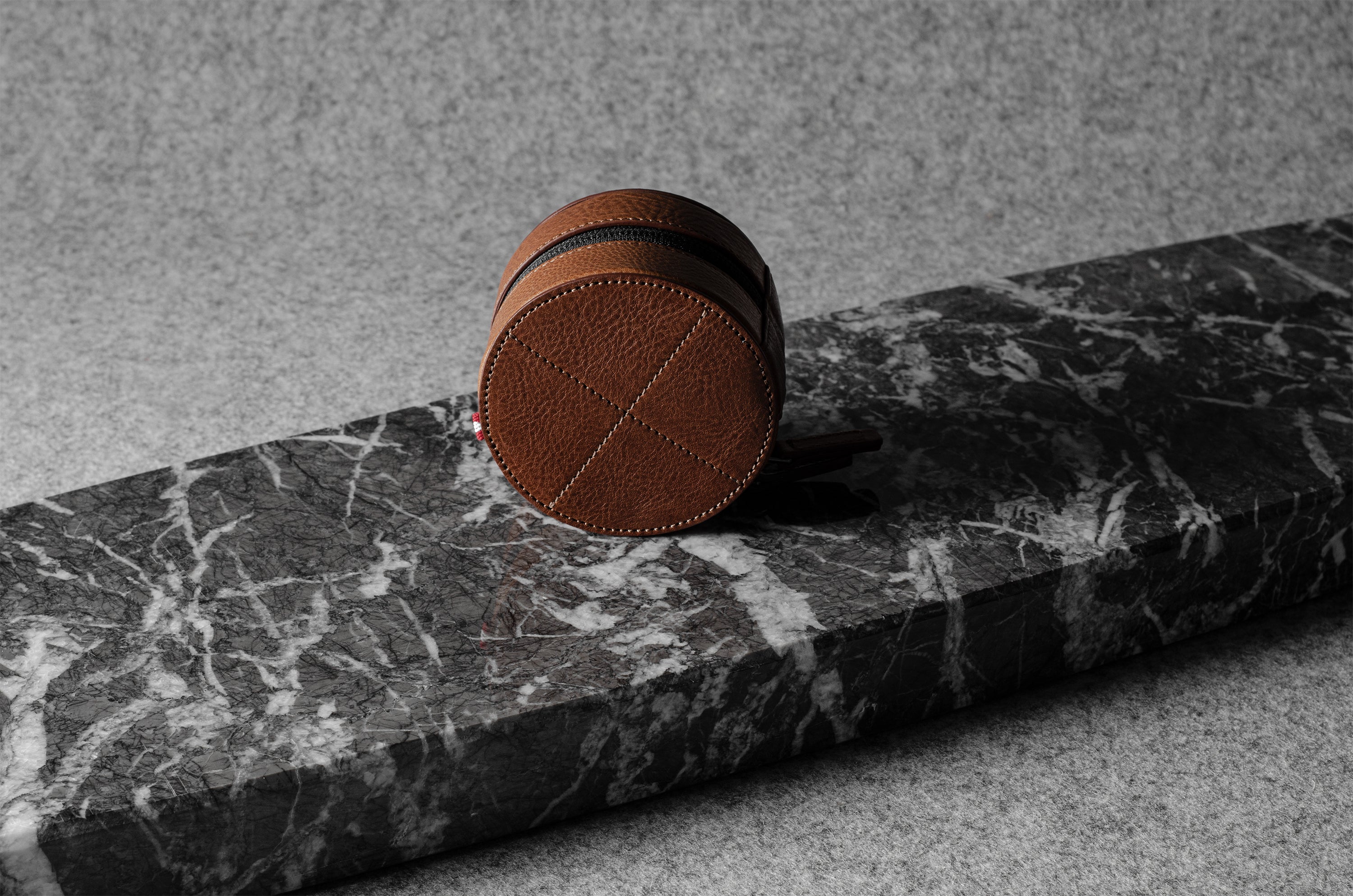 Brown leather watch case on a black marble surface with a gray background