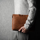 Person holding a brown leather laptop bag against a gray background