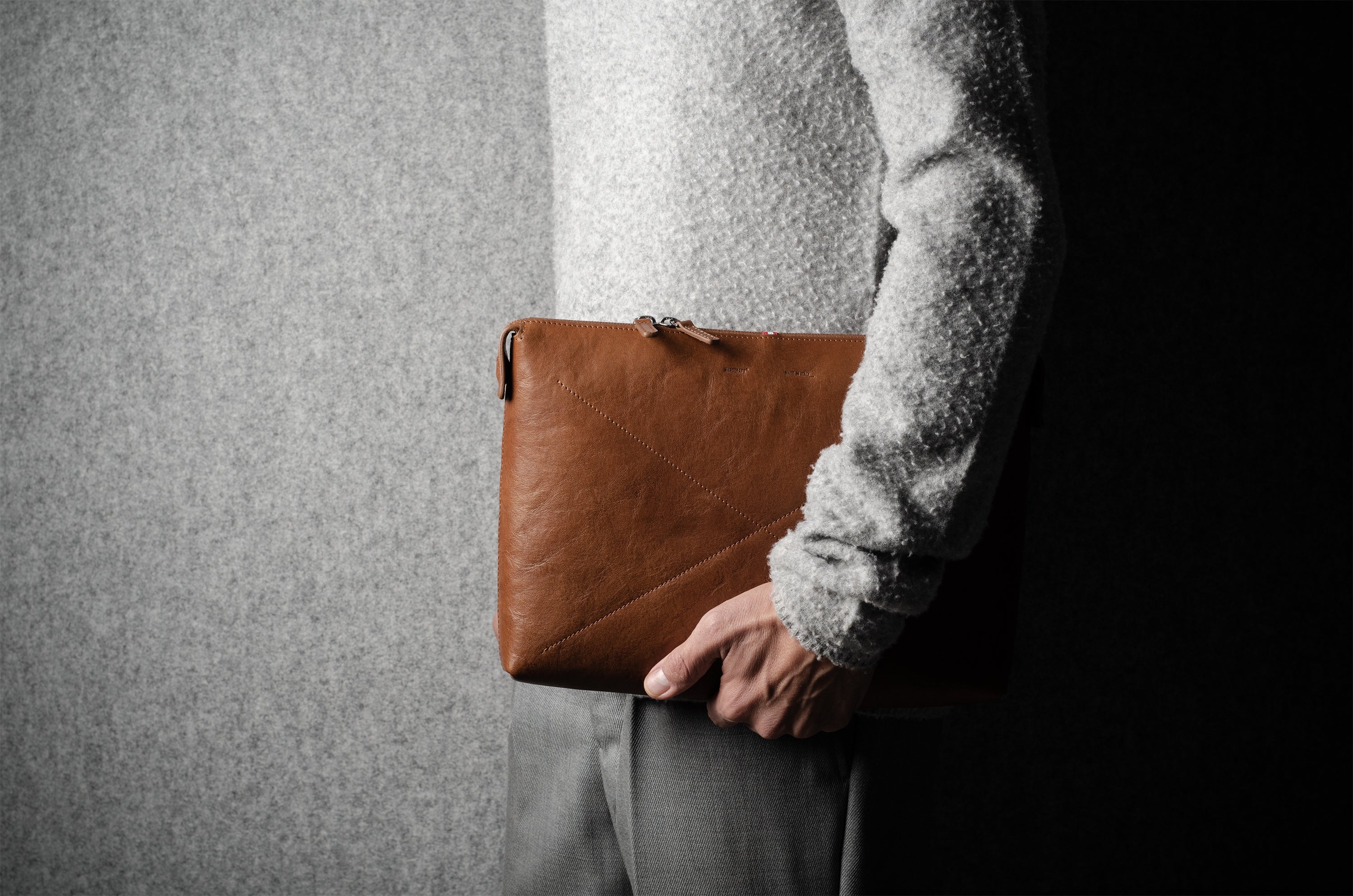 Person holding a brown leather laptop bag against a gray background