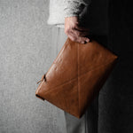 Person holding a brown leather laptop bag against a gray background