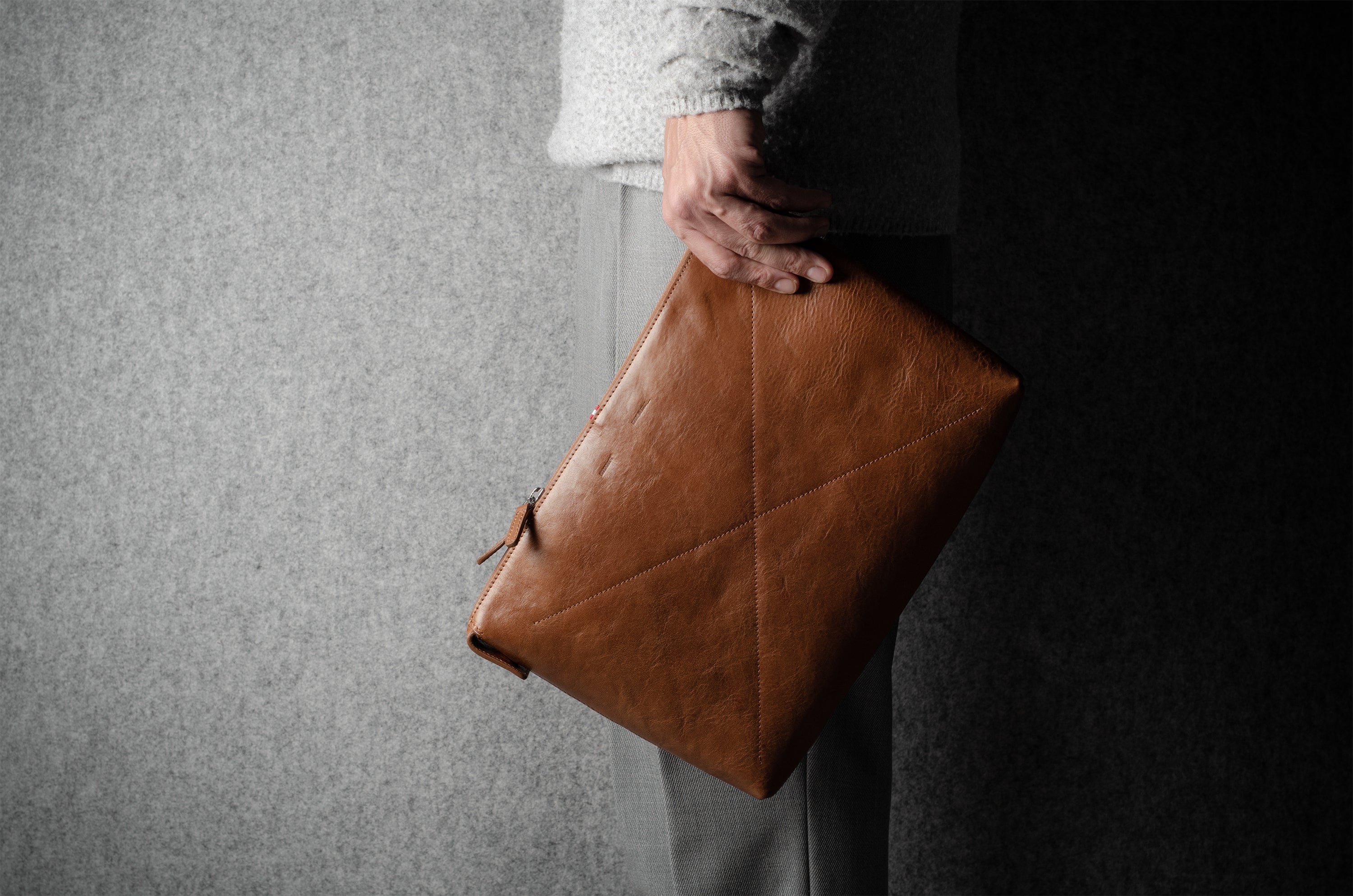 Person holding a brown leather laptop bag against a gray background