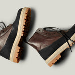 Pair of brown and black leather boots on a light gray background