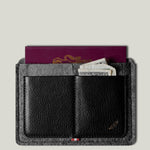 Black wallet with gray exterior holding a passport and money on a light gray background