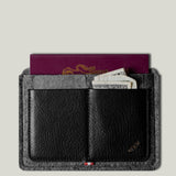 Black wallet with gray exterior holding a passport and money on a light gray background