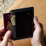 Person holding a black wallet and passport on a wooden surface