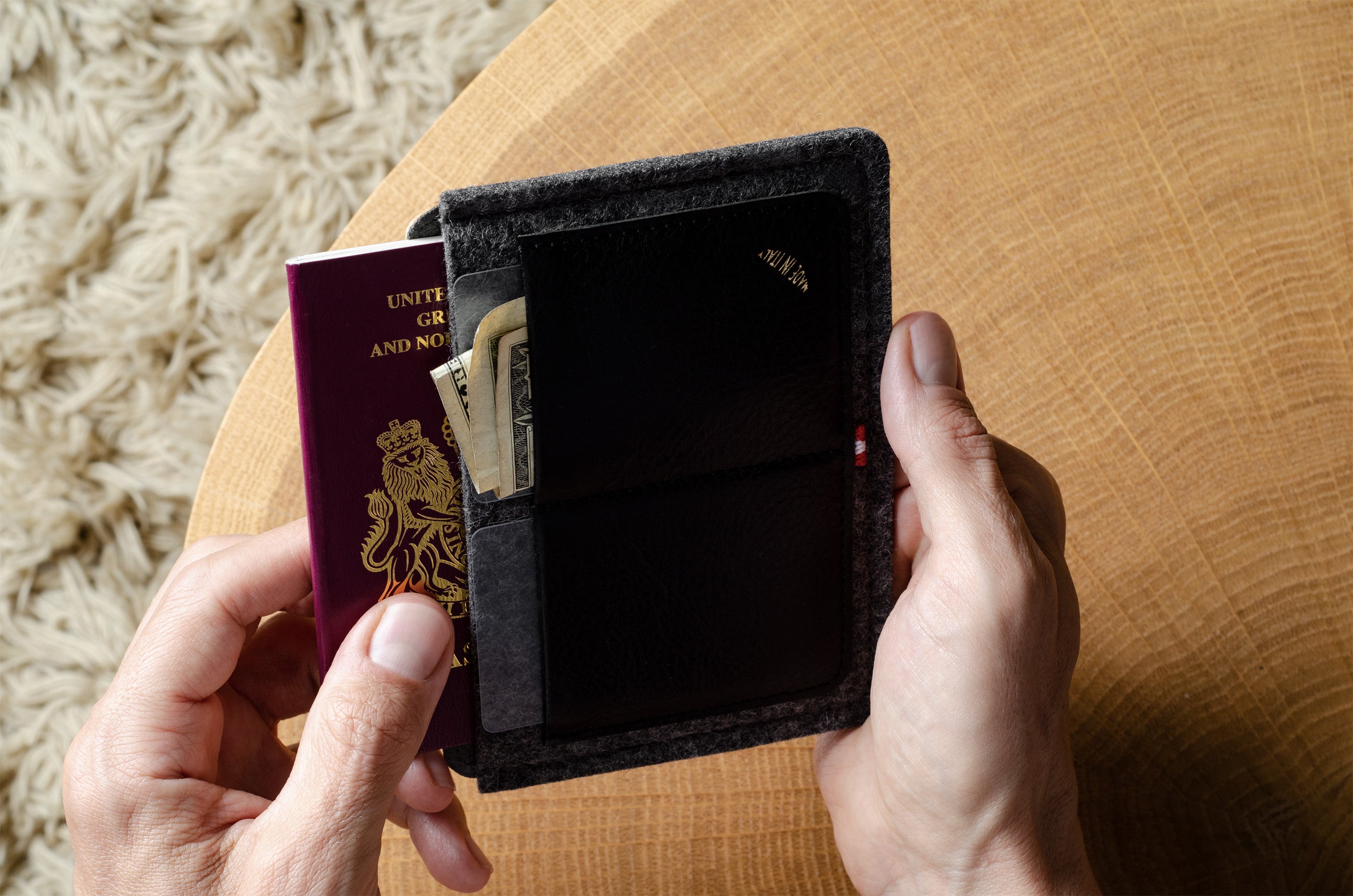 Person holding a black wallet and passport on a wooden surface