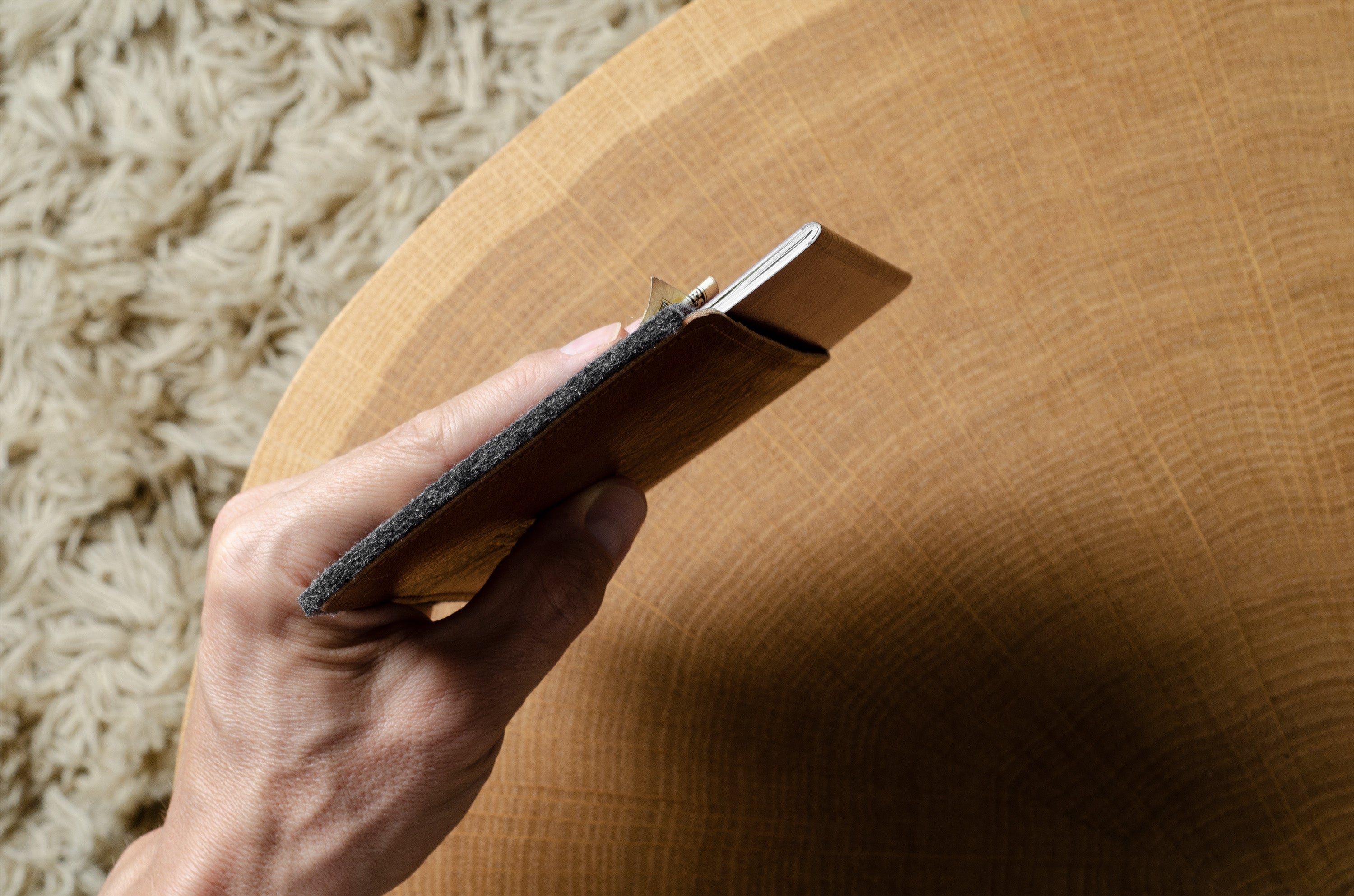 Hand holding a small leather-bound book on a wooden surface with a textured background