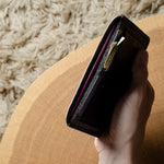 Hand holding a black passport wallet on a textured surface