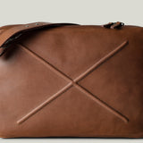Brown leather bag with X detail and shoulder strap.