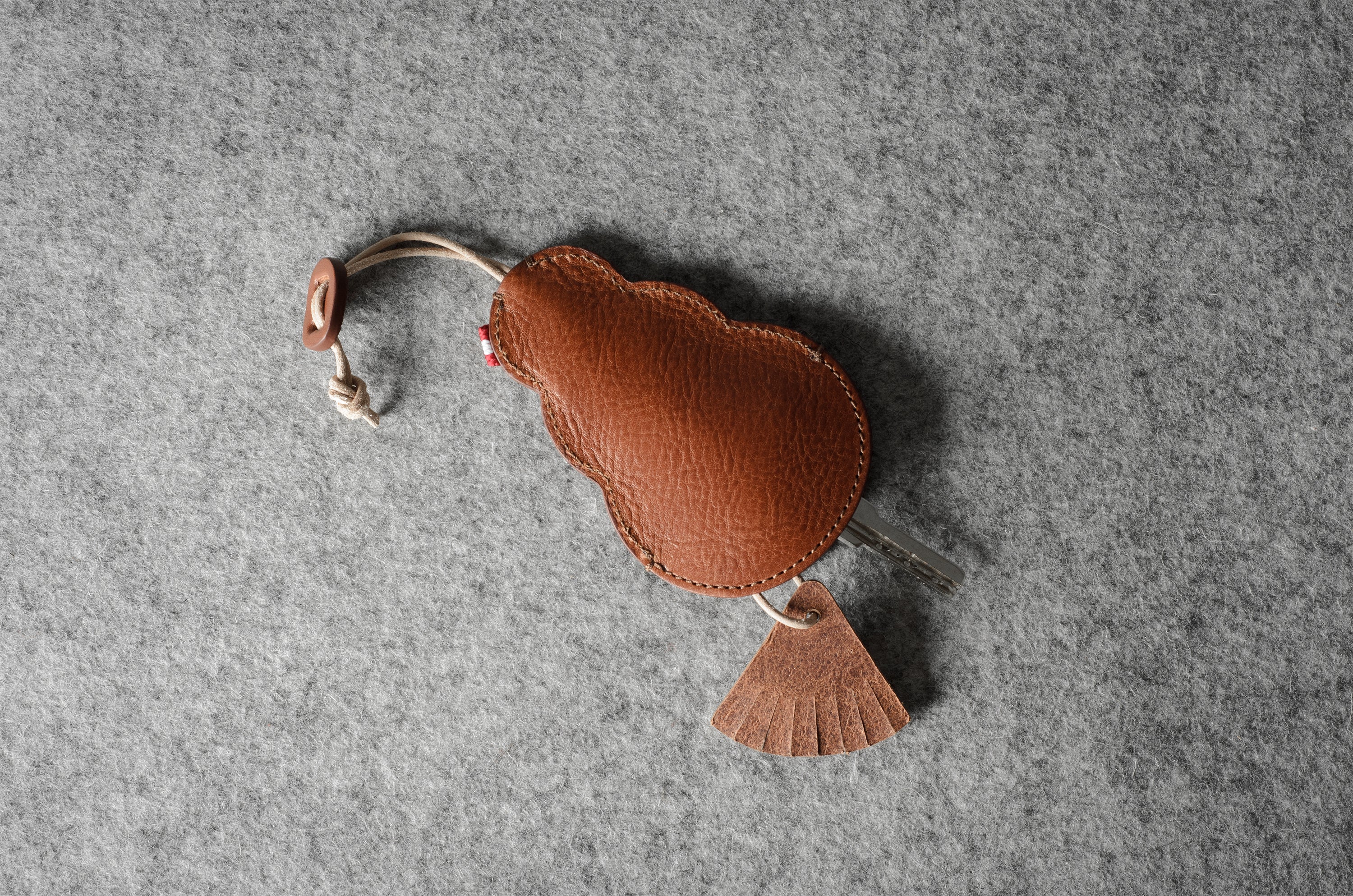Brown leather keypouch with a leather string on a gray background