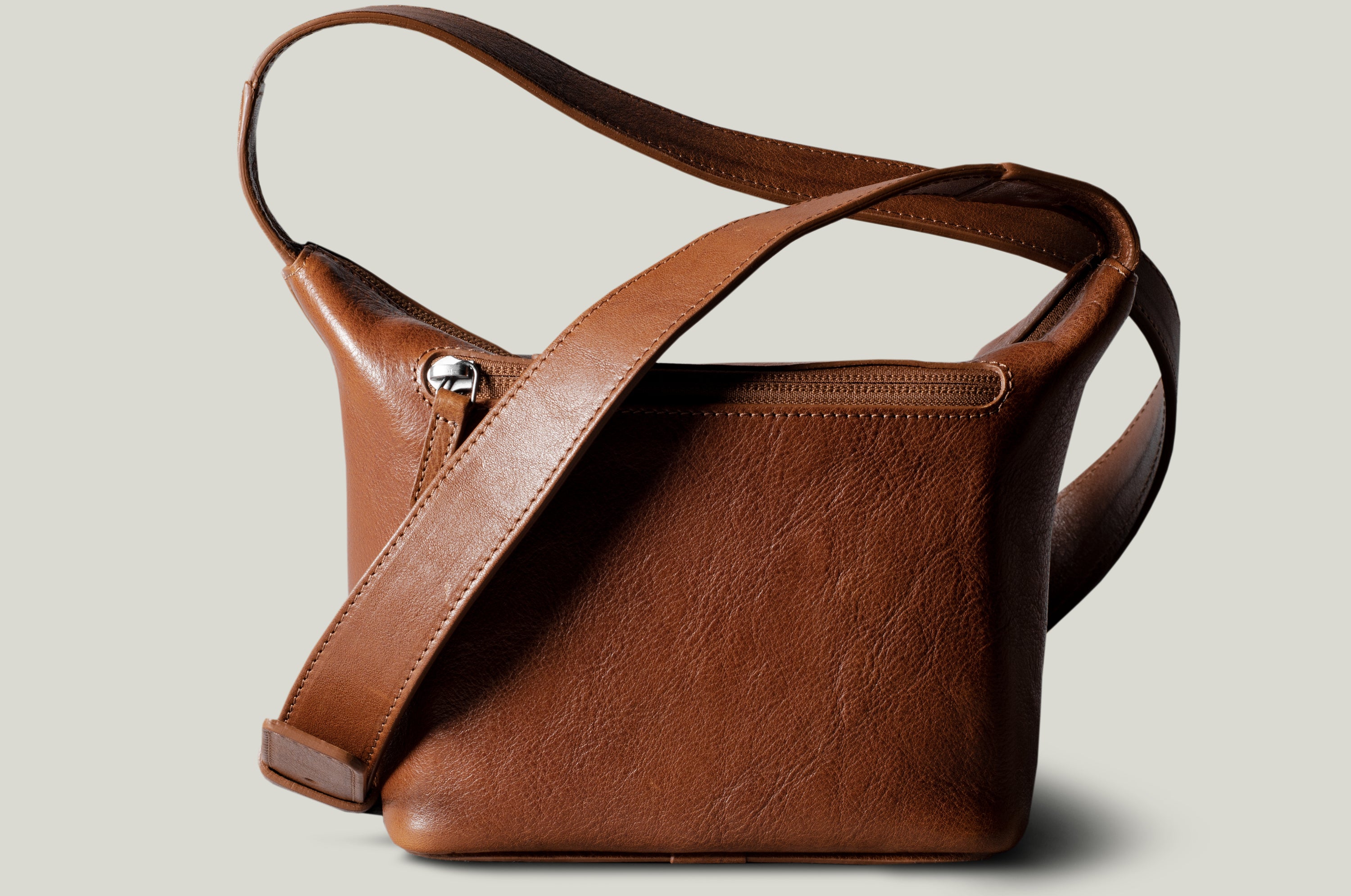 A classic brown leather camera bag with a shoulder strap and a zipper closure, viewed from the side.