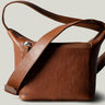 A classic brown leather camera bag with a shoulder strap and a zipper closure, viewed from the side.