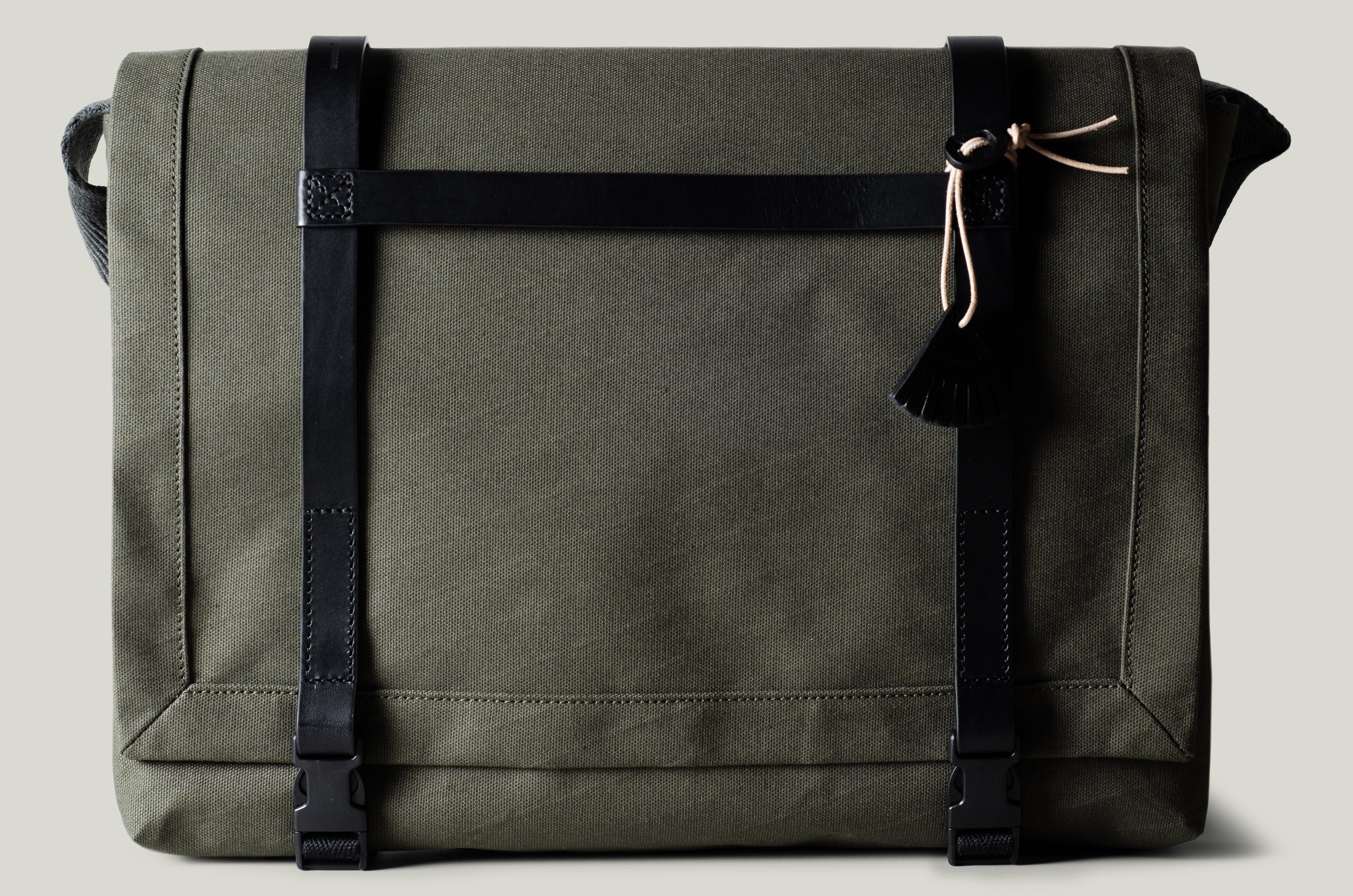 Green technical fabric messenger bag with black leather straps.
