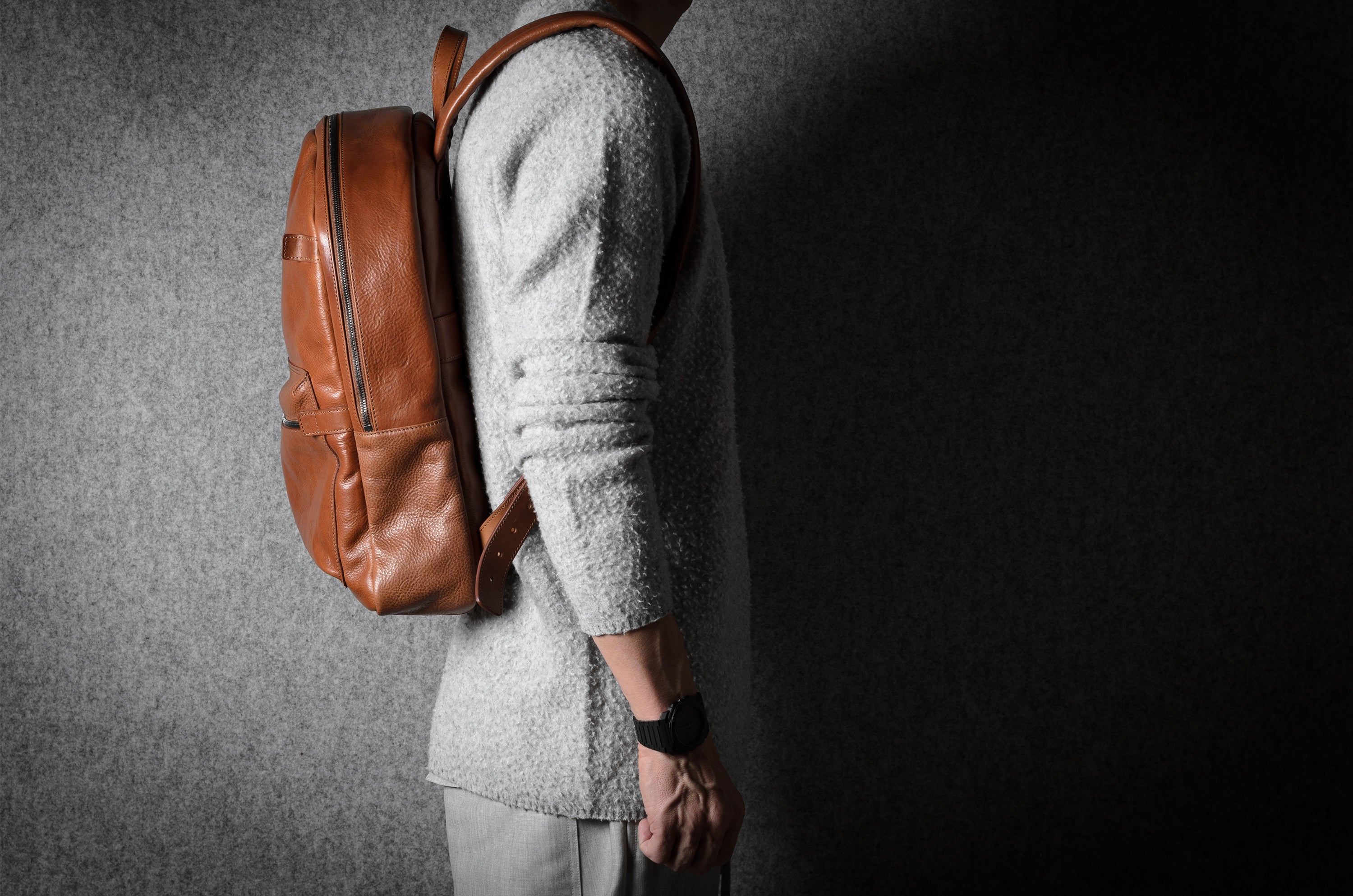 Person wearing a brown leather backpack against a dark background