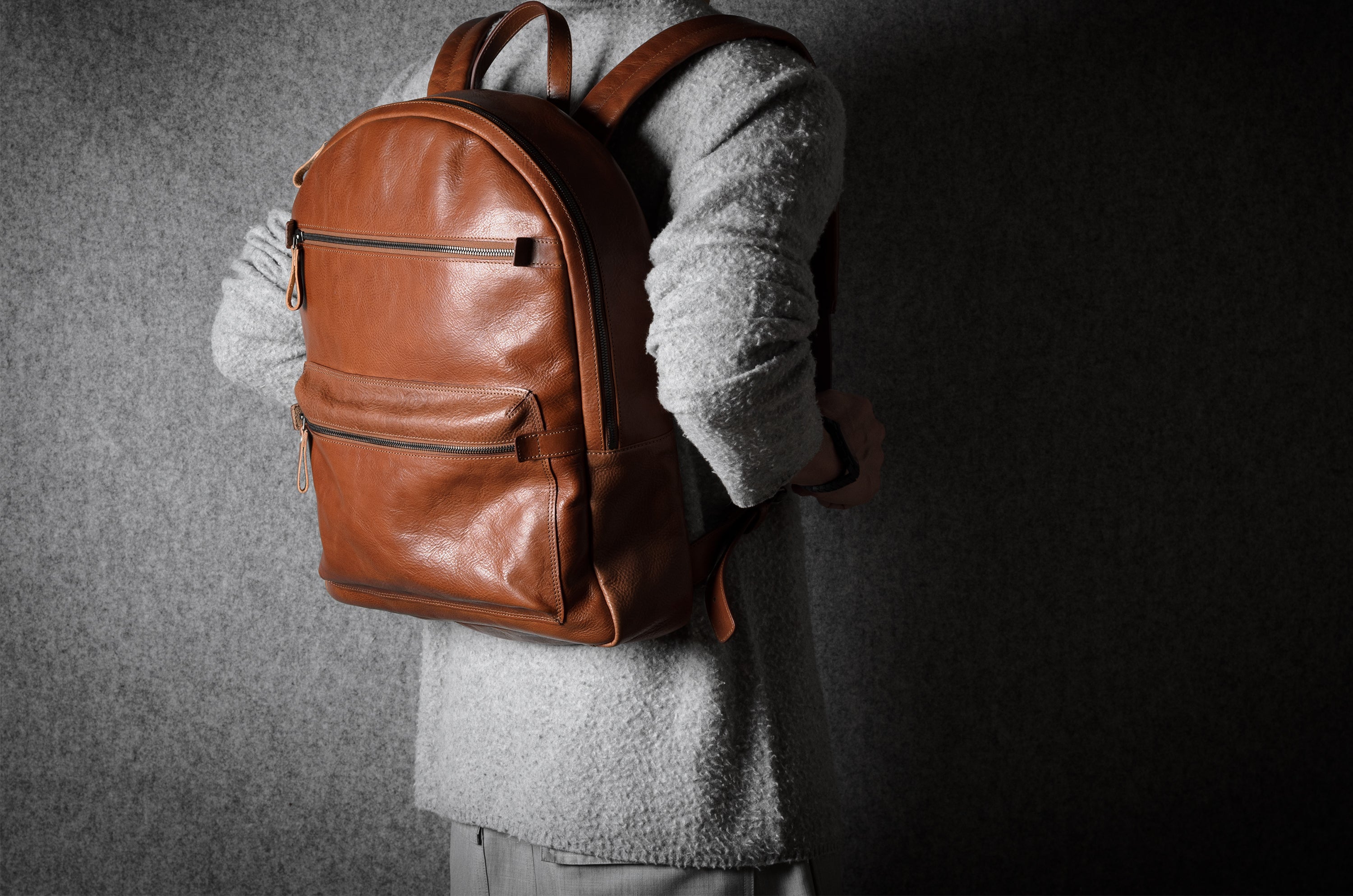 Person wearing a brown leather backpack against a dark background