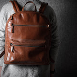 Brown leather backpack worn by a person on a dark background
