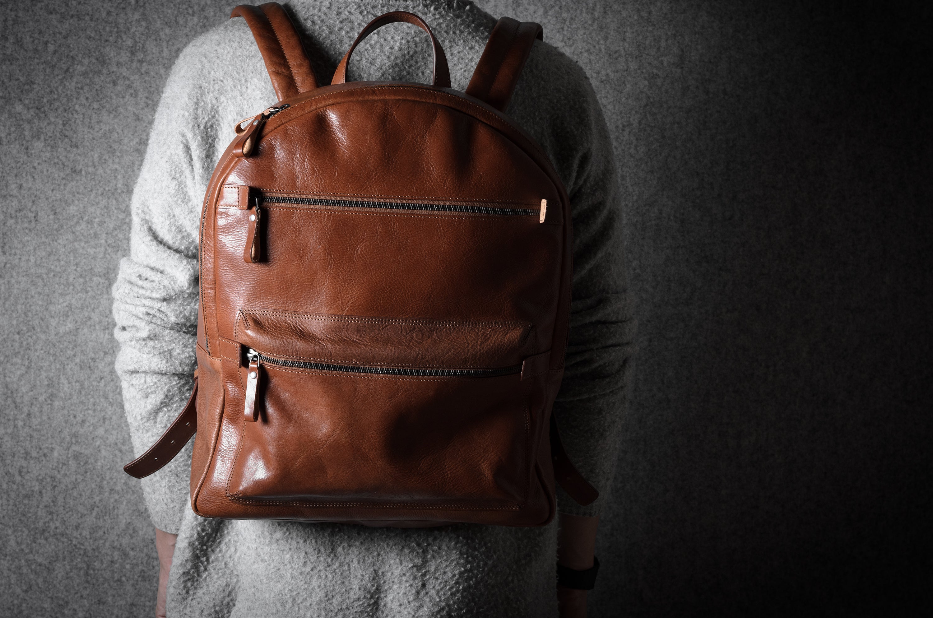 Brown leather backpack worn by a person on a dark background