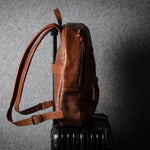 Brown leather backpack on a dark suitcase against a gray textured background