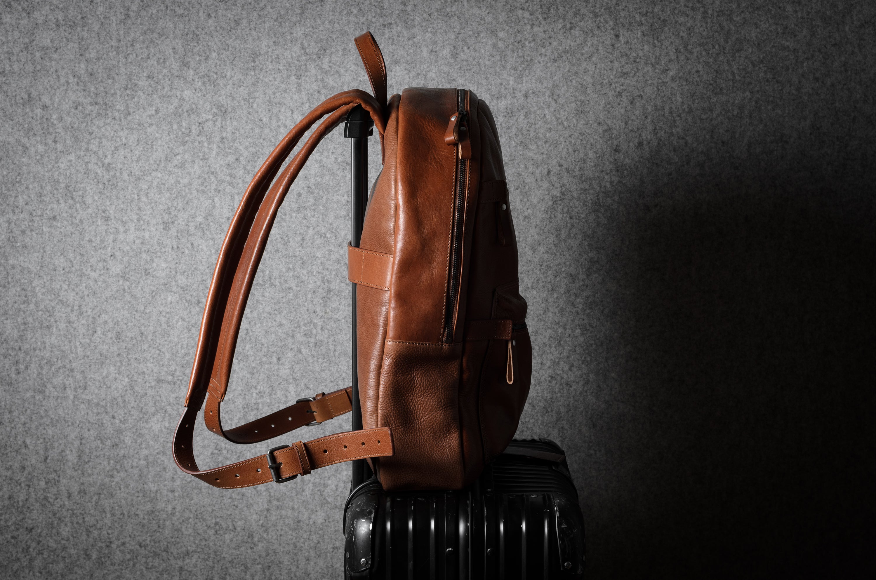 Brown leather backpack on a dark suitcase against a gray textured background