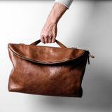 Brown leather bag held by a hand against a light background