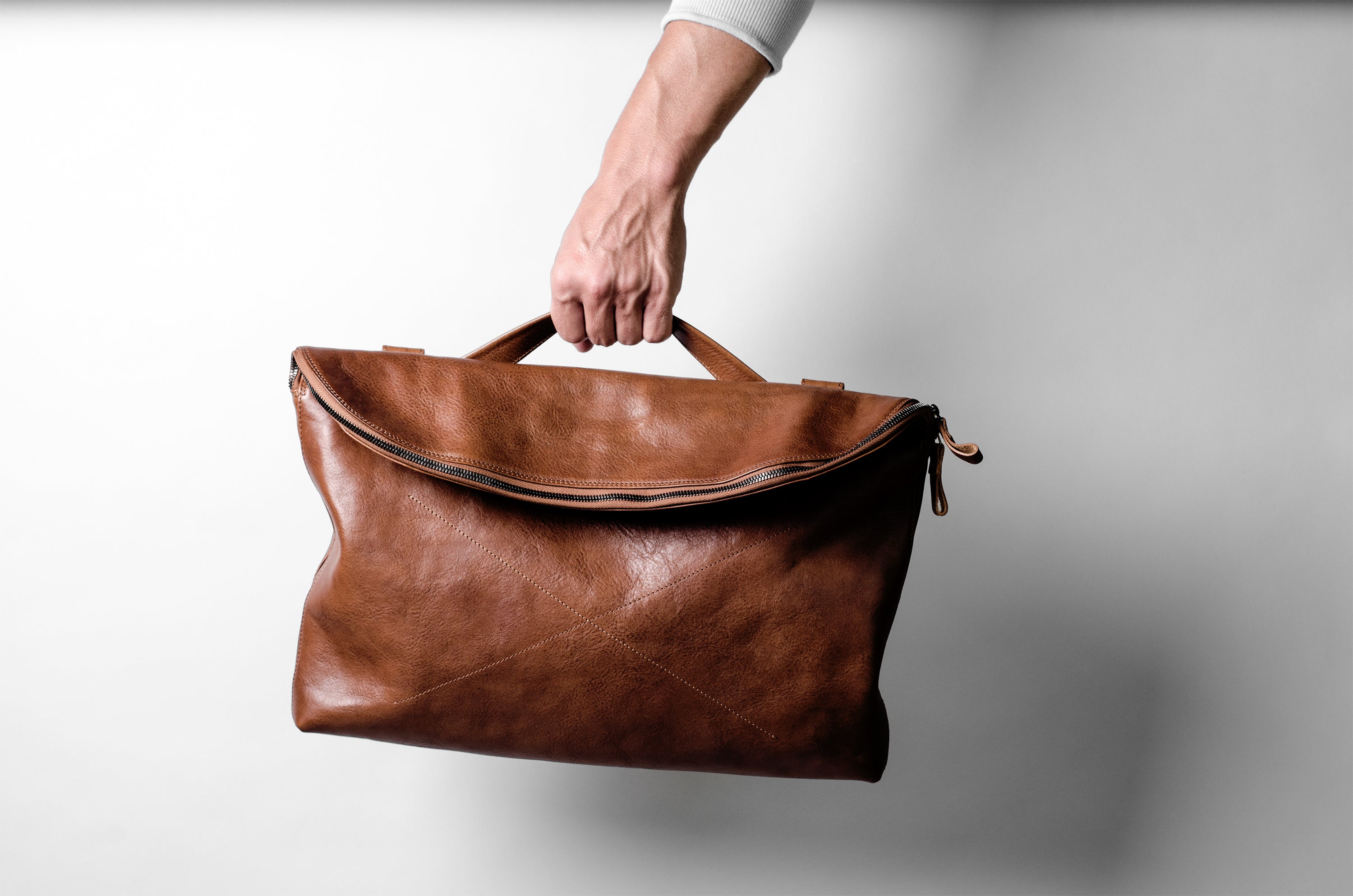 Brown leather bag held by a hand against a light background