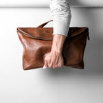 Brown leather bag held by a person against a white background