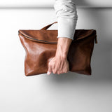Brown leather bag held by a person against a white background