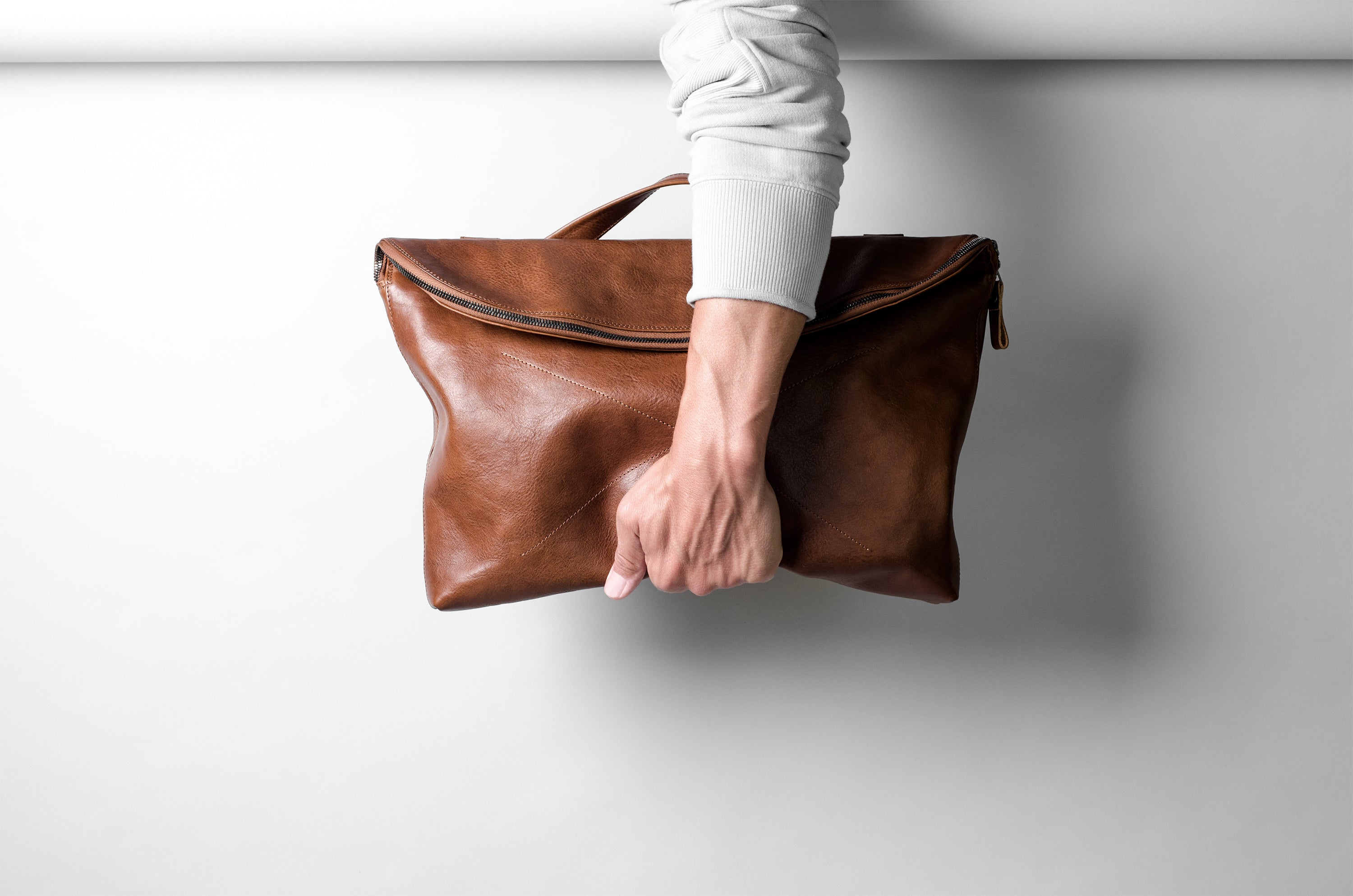 Brown leather bag held by a person against a white background