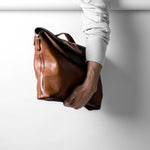 Brown leather handbag held by a person against a white background