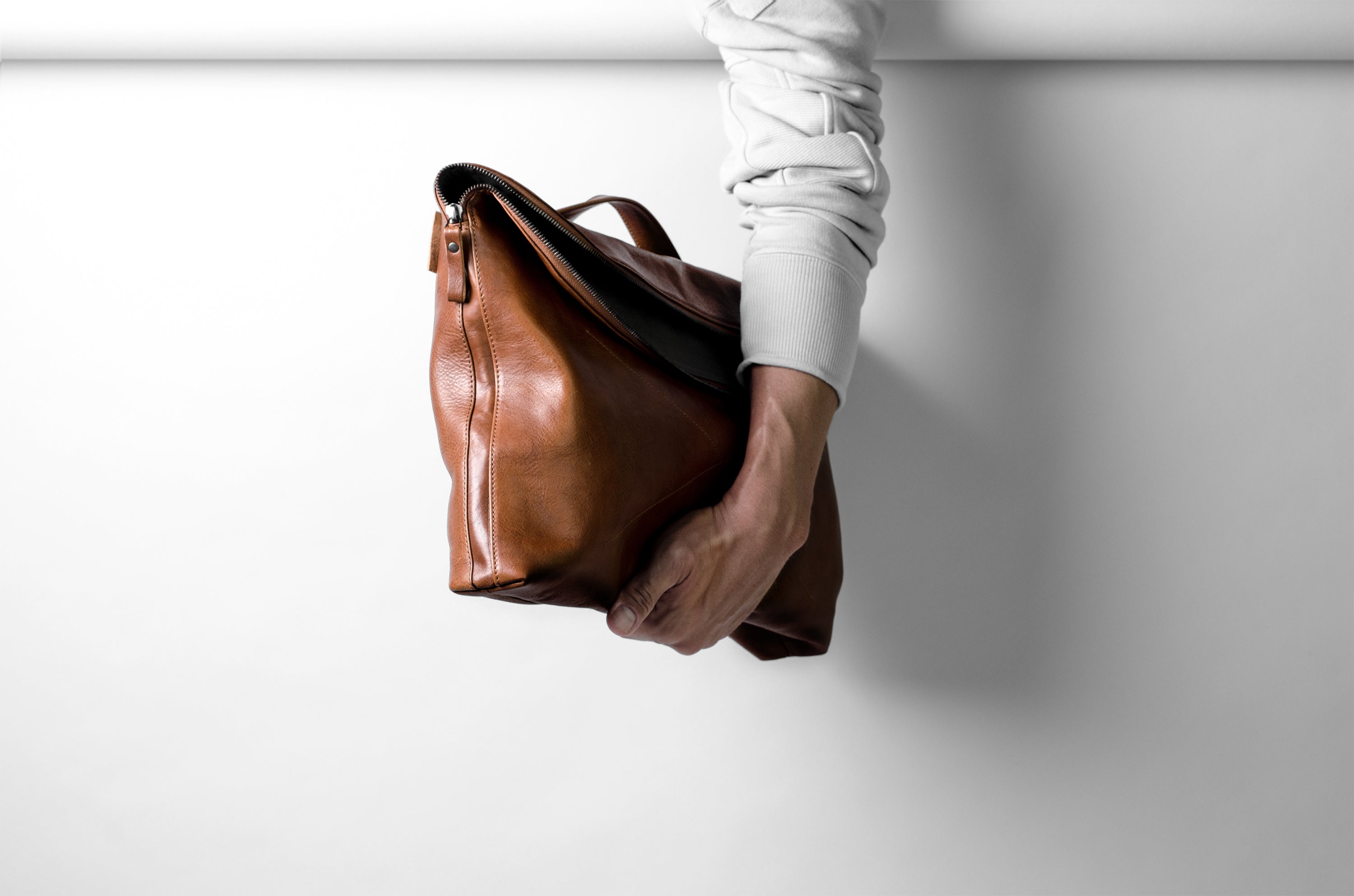 Brown leather handbag held by a person against a white background