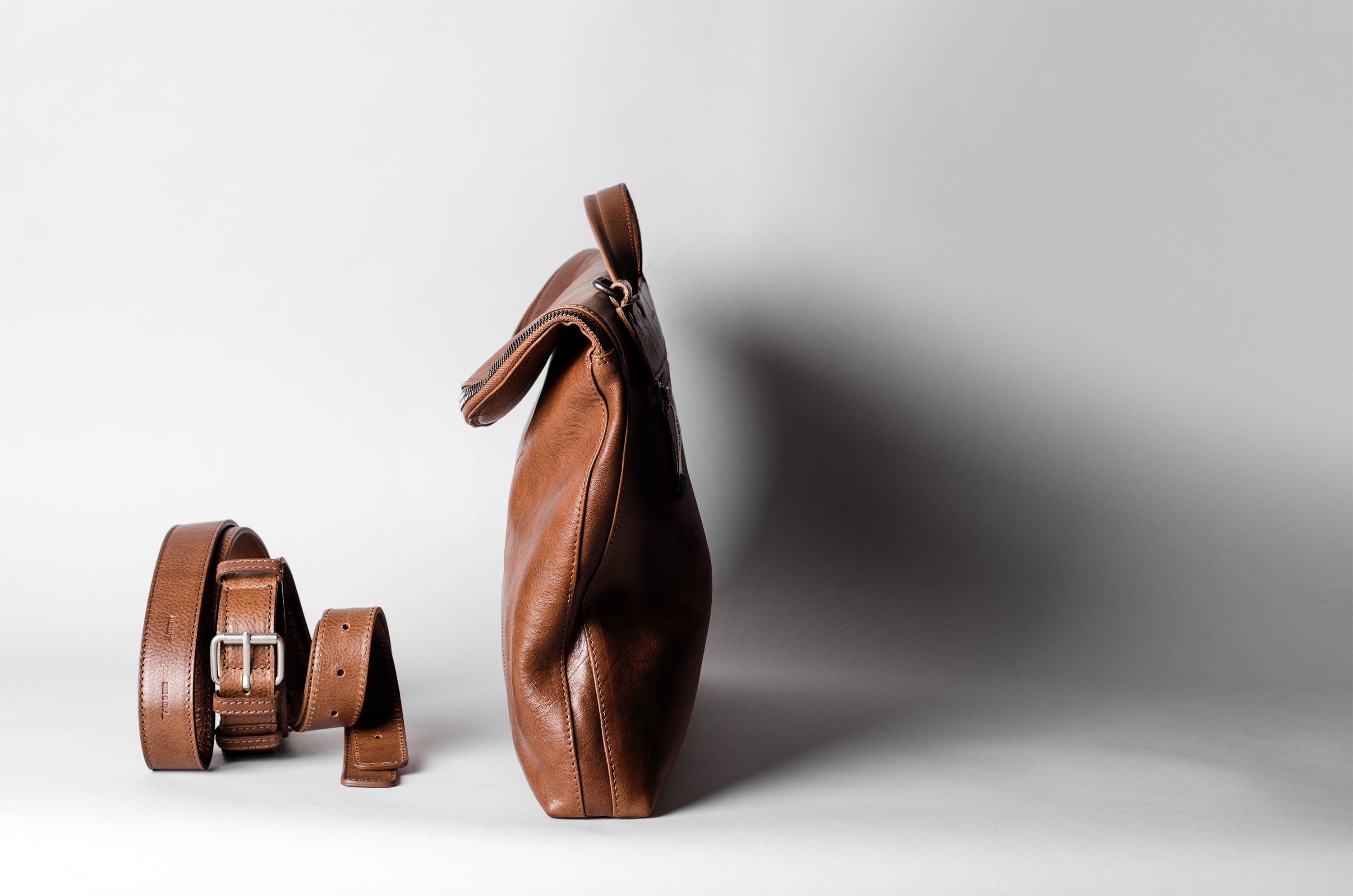 Brown leather bag and belt on a light gray background