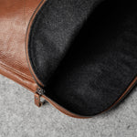 Brown leather bag with a dark grey interior on a gray surface