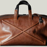 Brown leather duffel bag with black handles and strap on a light gray background