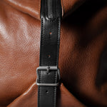 Brown leather bag with a black strap and buckle on a dark background