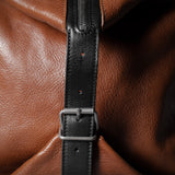 Brown leather bag with a black strap and buckle on a dark background