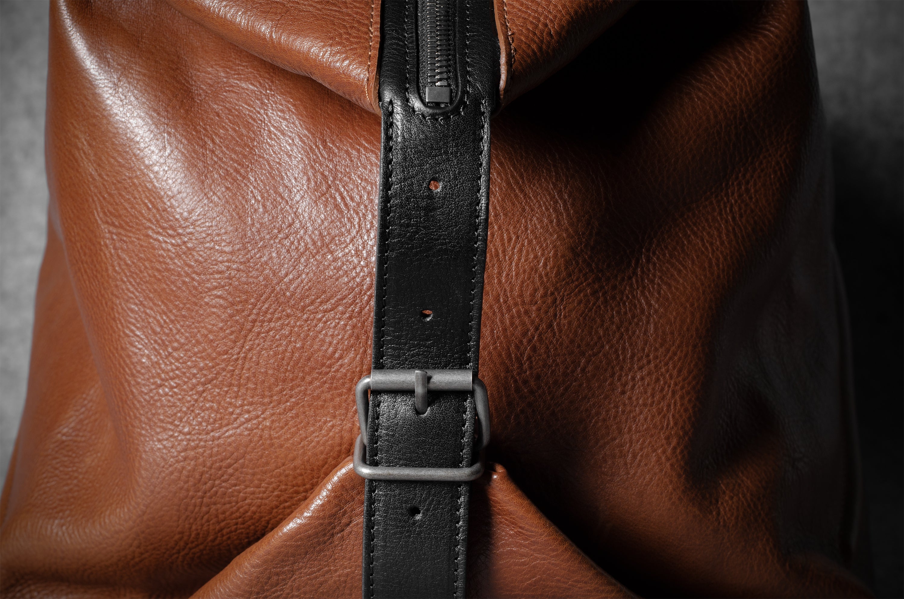 Brown leather bag with a black strap and buckle on a dark background
