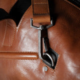 Close-up of a brown leather bag with a strap and buckle.