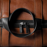 Close-up of a brown leather bag with black zipper and handle.